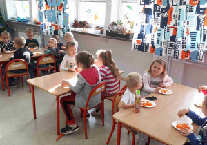 Dzieci siedza przy stolikach i zajadają przygotowaną surówkę